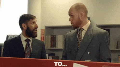 Two Men in Suits Standing Next to Each Other With Word To on Red Box