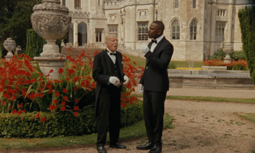 Two Men In Tuxedos Standing In Front Of A Large Building GIF