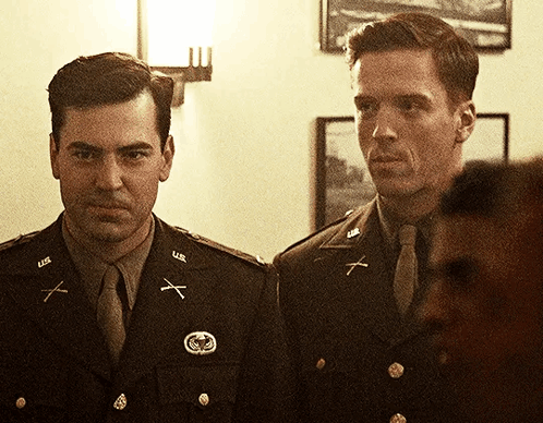 Two Men In U.s. Army Uniforms Are Standing Next To Each Other In A Room GIF