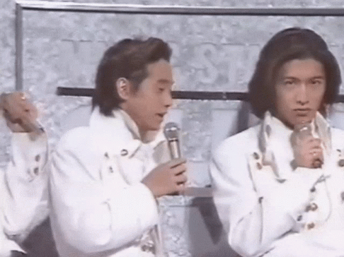Two Men In White Jackets Are Sitting Next To Each Other And Holding Microphones . GIF