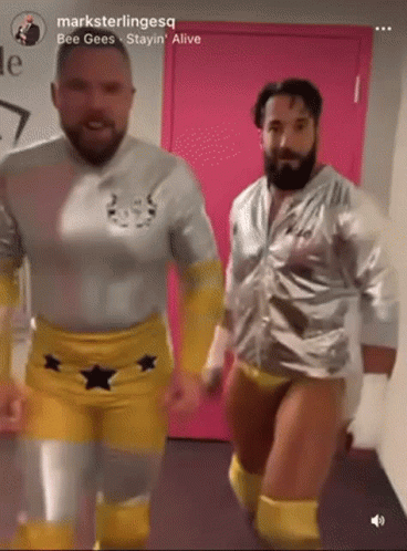 Two Men In Wrestling Outfits Are Dancing In Front Of A Pink Door With The Words " Bee Gees Stayin Alive " On The Bottom GIF