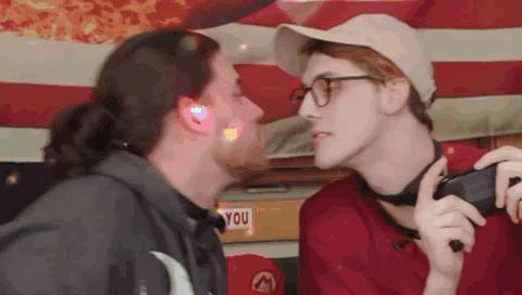 Two Men Kissing Under American Flag, One Wearing Glasses