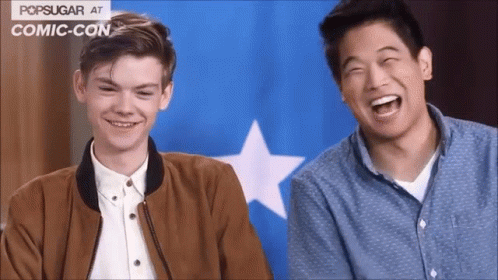Two Men Laughing In Front Of Blue And White Popsugar Flag At Comic Con GIF