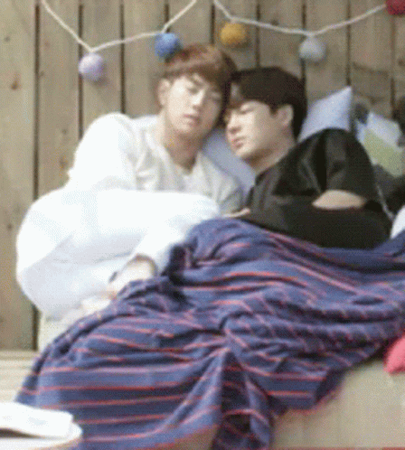 Two Men Laying on Bed With Striped Blanket