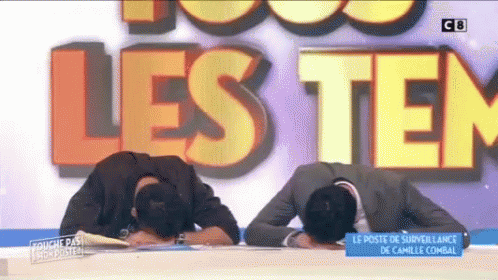 Two Men Laying Their Heads On A Table In Front Of A Large Sign That Says Les Tem GIF