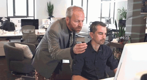 Two Men Looking At Computer Screen One Holding Cup GIF