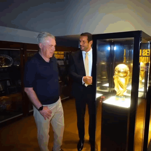 Two Men Looking at Trophy With Stadium Sign