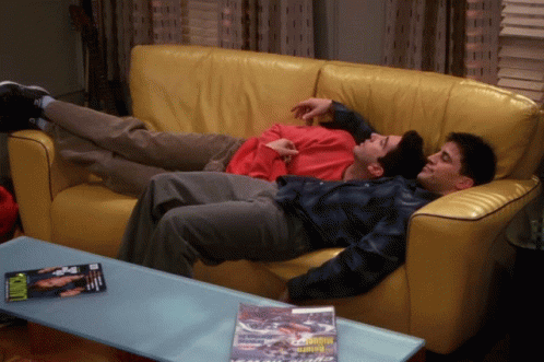 Two Men Lying On Yellow Couch With Motorcycle Magazine GIF