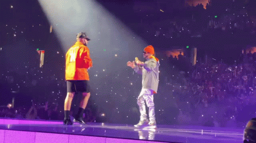 Two Men On A Stage With One Wearing An Orange Jacket With The Number 12 On It GIF