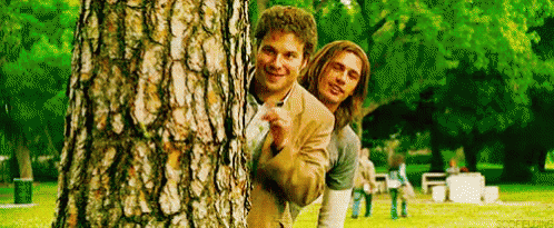 Two Men Peeking Behind Tree in Park