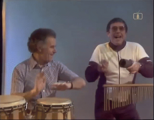 Two Men Playing Drums in Front of BBC TV Screen