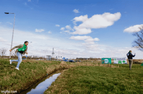 Two Men Playing Frisbee in Field With Recycling Sign