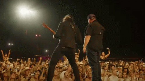 Two Men Playing Guitars In Front Of Crowd GIF