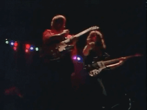 Two Men Playing Guitars On Stage With 'A' Shirt