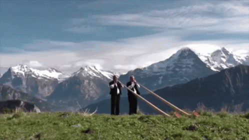 Two Men Playing Horns in Front of Mountain Range