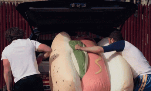 Two Men Pushing Giant Hot Dog in Car