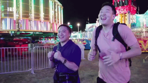 Two Men Running And Laughing Near Carnival Ride GIF