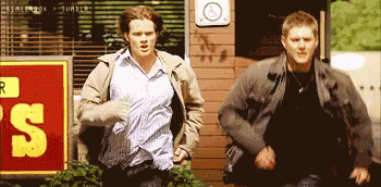 Two Men Running Past Sign 's