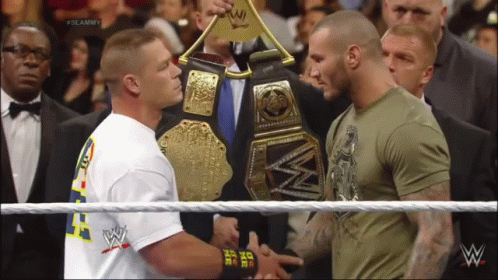 Two Men Shaking Hands In A Wrestling Ring With One Wearing A Shirt That Says ' I Am The One ' On It GIF