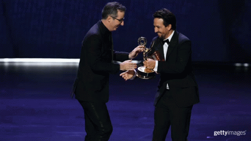 Two Men Shaking Hands On A Stage While One Holds A Trophy GIF