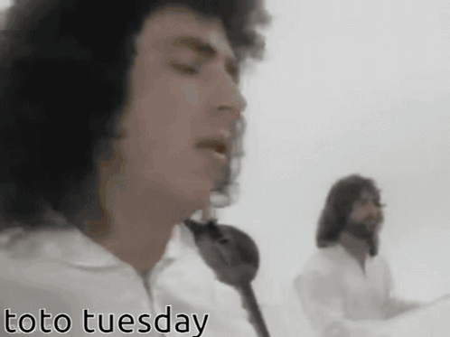 Two Men Singing In Front Of A White Background With Toto Tuesday In The Corner GIF