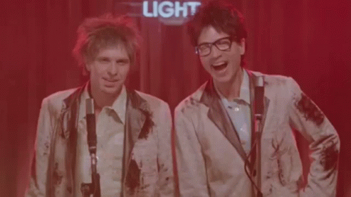 Two Men Singing Into Microphones Under Light Sign GIF