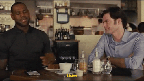 Two Men Sit At A Table In A Restaurant And One Of Them Says " Listen " GIF