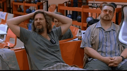 Two Men Sit In A Bowling Alley With Their Hands On Their Head GIF