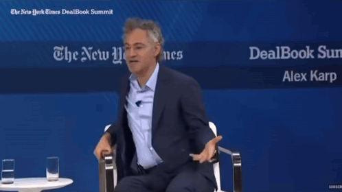 Two Men Sit In Front Of A Sign That Says Dealbook Summit GIF