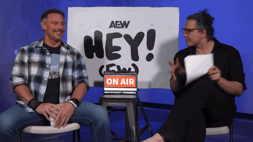 two men sit in front of a sign that says hey on air