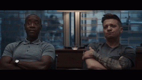 Two Men Sit With Their Arms Crossed And One Has A Tattoo On His Arm GIF