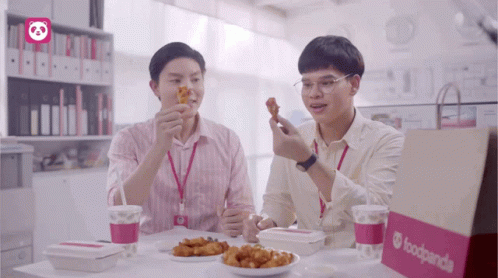 Two Men Sitting At A Table Eating Food From A Foodpanda Bag GIF