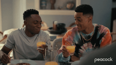 Two Men Sitting At A Table With Peacock Written On The Bottom Left GIF