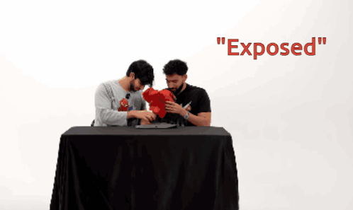 Two Men Sitting At A Table With The Word Exposed On The Wall GIF