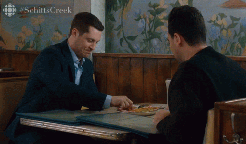 Two Men Sitting at Schitt's Creek Sign