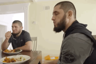Two Men Sitting At Table Eating Food One With Beard GIF