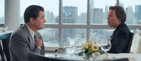 Two Men Sitting at Table in Front of Large Window Talking