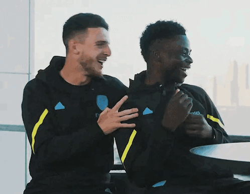 Two Men Sitting At Table With Emirates Sweatshirt GIF