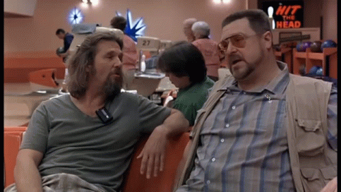 Two Men Sitting In A Bowling Alley With A Sign That Says Hit The Head GIF
