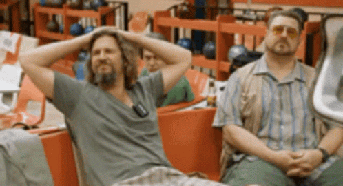 Two Men Sitting In A Bowling Alley With Their Hands On Their Heads GIF