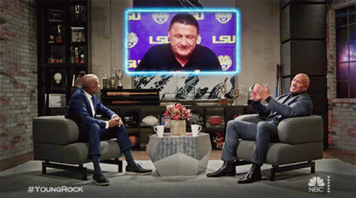 Two Men Sitting in Chairs before LSU Screen