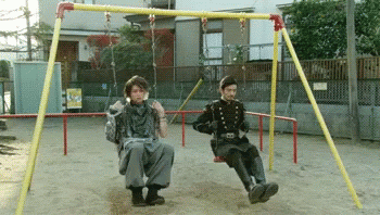 Two Men Sitting On A Swing Set In A Park GIF