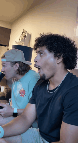 Two Men Sitting On Couch One In Top Hat One In Black Shirt GIF