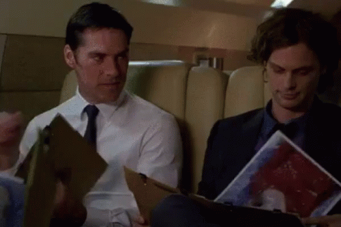 Two Men Sitting on Plane One Holding Clipboard