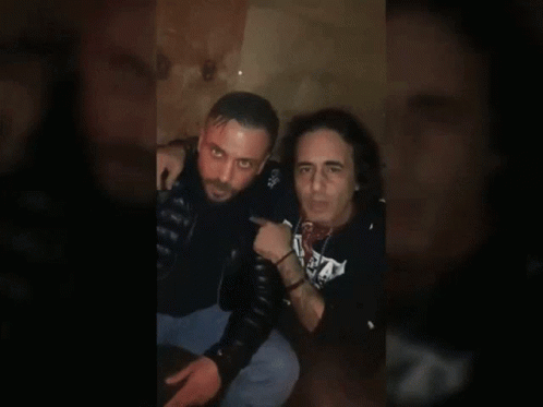 Two Men Sitting, One In S.A. Shirt GIF