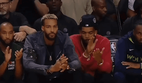 Two Men Sitting, One Wearing NBA Hat GIF