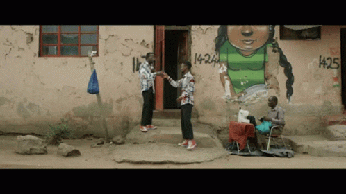 Two Men Standing In Front Of A Building With Graffiti On It That Says 1425 GIF