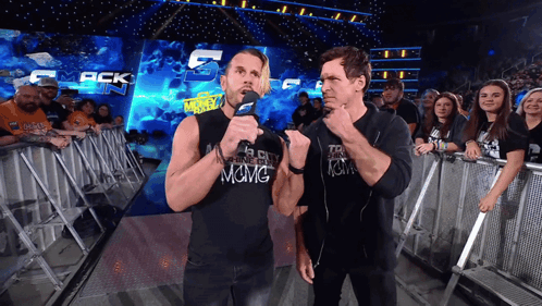 Two Men Standing In Front Of A Crowd With One Wearing A Shirt That Says Among GIF