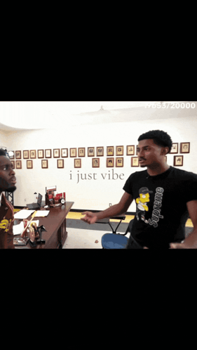 Two Men Standing In Front Of A Wall That Says I Just Vibe On It GIF