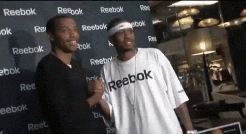 Two Men Standing In Front Of A Wall That Says Reebok On It GIF